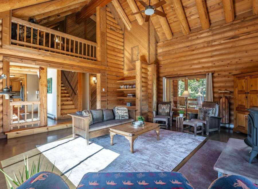 Experience rustic charm in this stunning log cabin living room, featuring a grand stone fireplace and soaring vaulted ceilings with exposed beams.