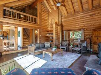 Experience rustic charm in this stunning log cabin living room, featuring a grand stone fireplace and soaring vaulted ceilings with exposed beams.