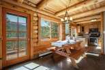 Experience rustic charm in this log cabin dining area, featuring a wooden picnic table set for a meal with stunning mountain views through large windows.