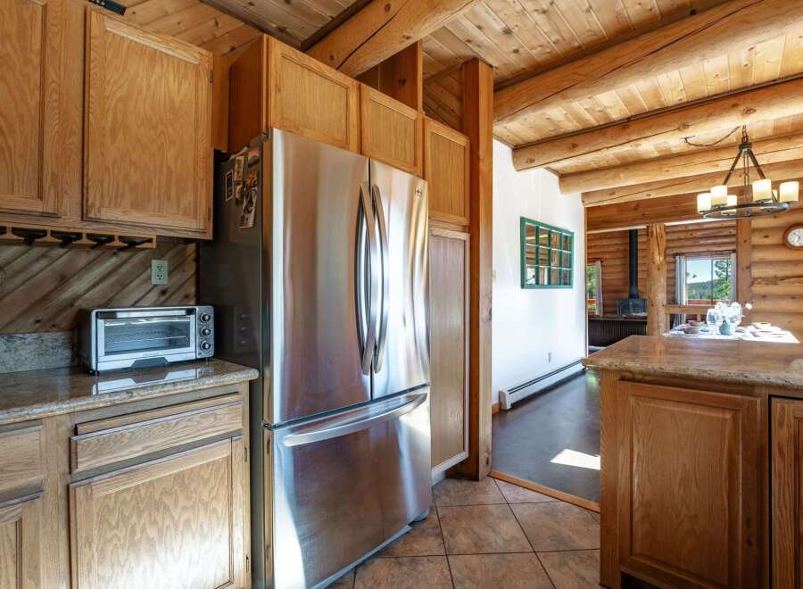 Experience rustic charm in this log cabin kitchen featuring a spacious stainless steel refrigerator and ample wooden cabinetry.