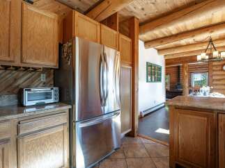 Experience rustic charm in this log cabin kitchen featuring a spacious stainless steel refrigerator and ample wooden cabinetry.