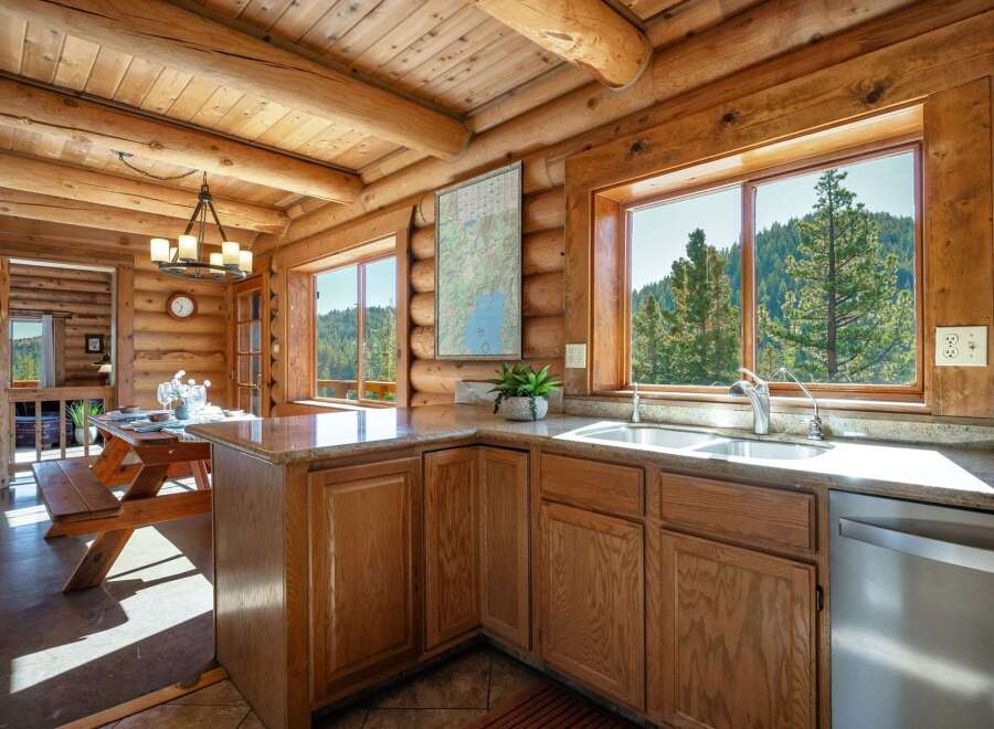 Experience rustic charm in this log cabin kitchen, featuring a spacious picnic table dining area and stunning mountain views through large windows.