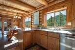 Experience rustic charm in this log cabin kitchen, featuring a spacious picnic table dining area and stunning mountain views through large windows.