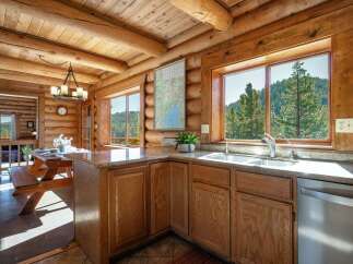 Experience rustic charm in this log cabin kitchen, featuring a spacious picnic table dining area and stunning mountain views through large windows.
