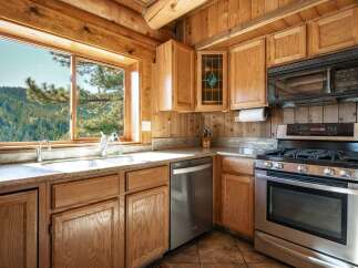 Experience rustic charm in this cozy log cabin kitchen, featuring beautiful natural wood cabinetry and a stunning stained-glass accent cabinet.