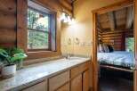 Experience rustic charm in this log cabin bathroom featuring a granite-topped vanity and a large window with picturesque forest views.