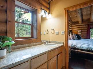 Experience rustic charm in this log cabin bathroom featuring a granite-topped vanity and a large window with picturesque forest views.