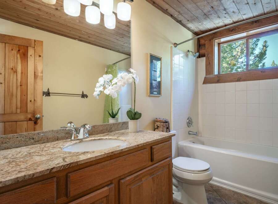 This rustic bathroom features a charming wooden door and ceiling, complemented by a granite countertop and a white vessel sink.