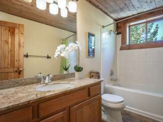 This rustic bathroom features a charming wooden door and ceiling, complemented by a granite countertop and a white vessel sink.