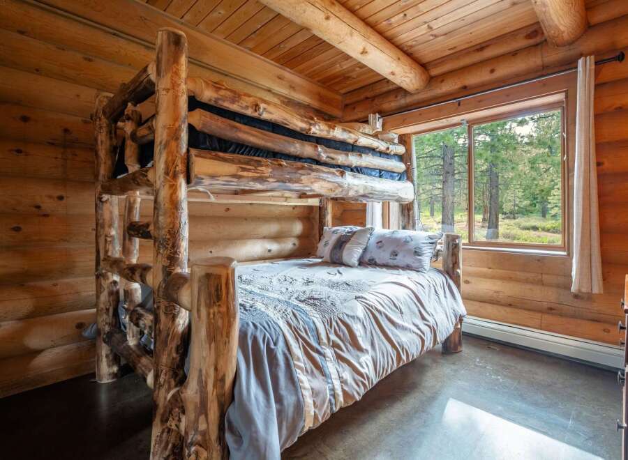 Experience rustic charm in this cozy log cabin bedroom, featuring a unique, handcrafted log bunk bed and a comfortable lower bunk dressed in soft linens.