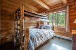 Experience rustic charm in this cozy log cabin bedroom, featuring a unique, handcrafted log bunk bed and a comfortable lower bunk dressed in soft linens.