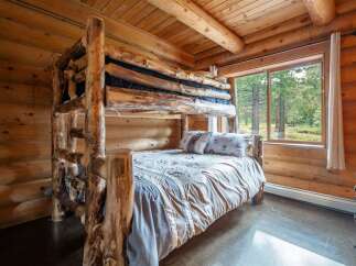 Experience rustic charm in this cozy log cabin bedroom, featuring a unique, handcrafted log bunk bed and a comfortable lower bunk dressed in soft linens.