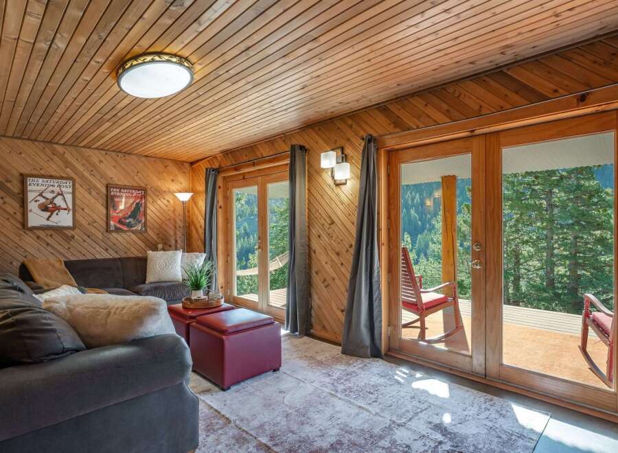 Experience breathtaking mountain views from this cozy living room, featuring warm wood paneling and a comfortable sectional sofa.