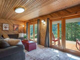 Experience breathtaking mountain views from this cozy living room, featuring warm wood paneling and a comfortable sectional sofa.