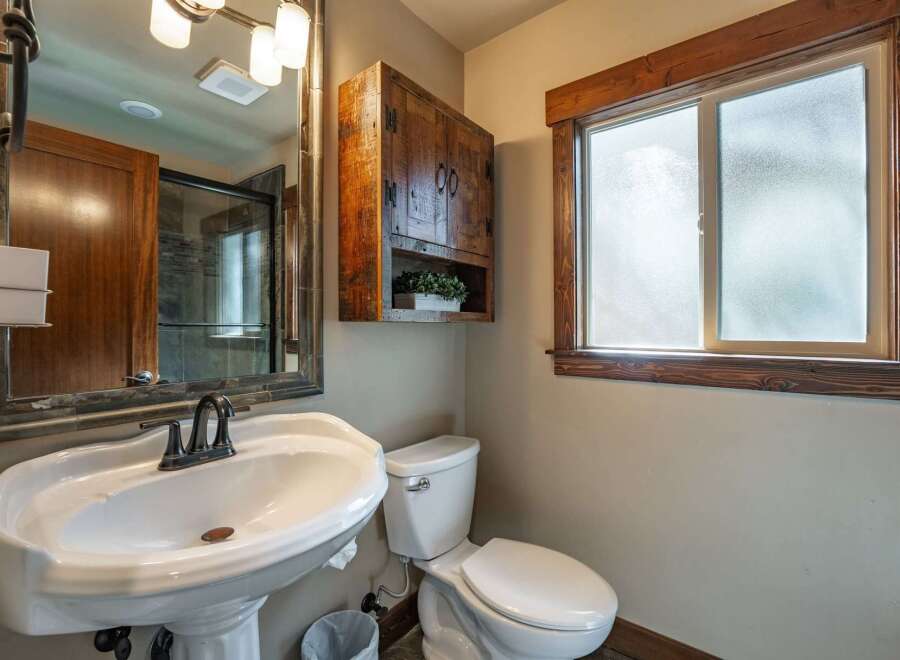 This rustic bathroom features a charming wooden cabinet above a pedestal sink and toilet.