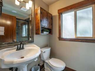 This rustic bathroom features a charming wooden cabinet above a pedestal sink and toilet.