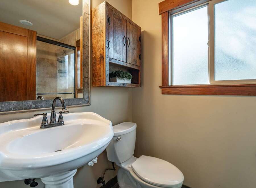 This charming bathroom features a pedestal sink with a vintage-inspired faucet, complemented by a rustic wooden medicine cabinet.