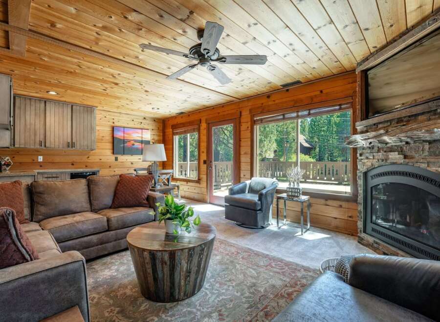 Experience rustic charm in this cozy living room featuring a stunning stone fireplace and a warm, wood-paneled ceiling.