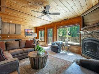 Experience rustic charm in this cozy living room featuring a stunning stone fireplace and a warm, wood-paneled ceiling.