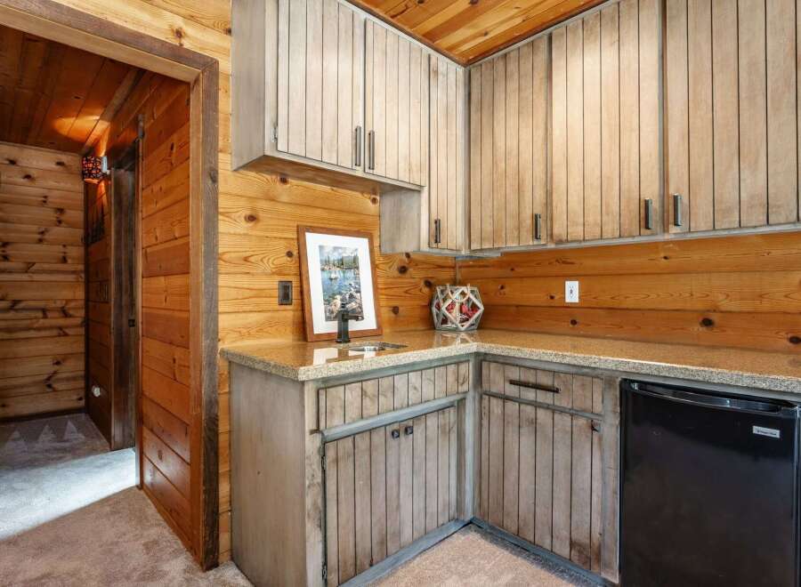 This charming rustic kitchen features warm wood paneling throughout, complemented by light-colored cabinetry and granite countertops.