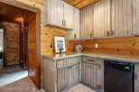 This charming rustic kitchen features warm wood paneling throughout, complemented by light-colored cabinetry and granite countertops.