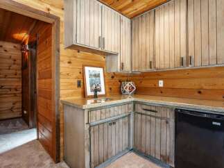 This charming rustic kitchen features warm wood paneling throughout, complemented by light-colored cabinetry and granite countertops.
