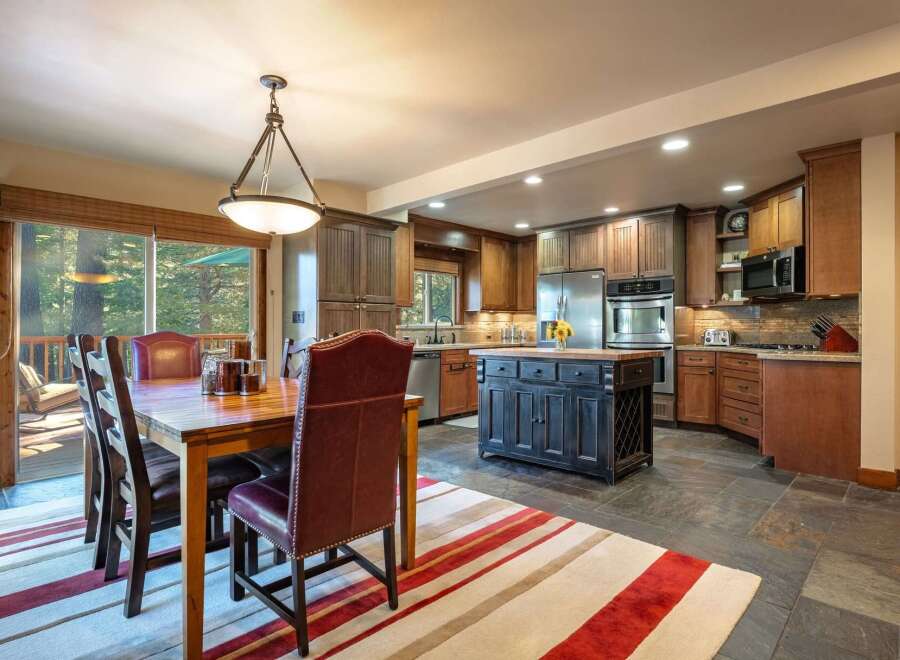 Experience comfortable dining and cooking in this spacious kitchen and dining area, featuring a large wooden dining table with plush seating and a well-equipped kitchen with a central island.