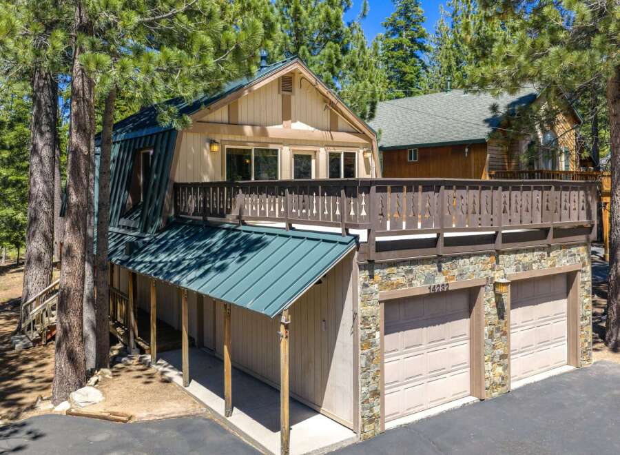 Nestled among tall pine trees, this charming home offers a unique A-frame design with a striking green metal roof.