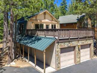 Nestled among tall pine trees, this charming home offers a unique A-frame design with a striking green metal roof.