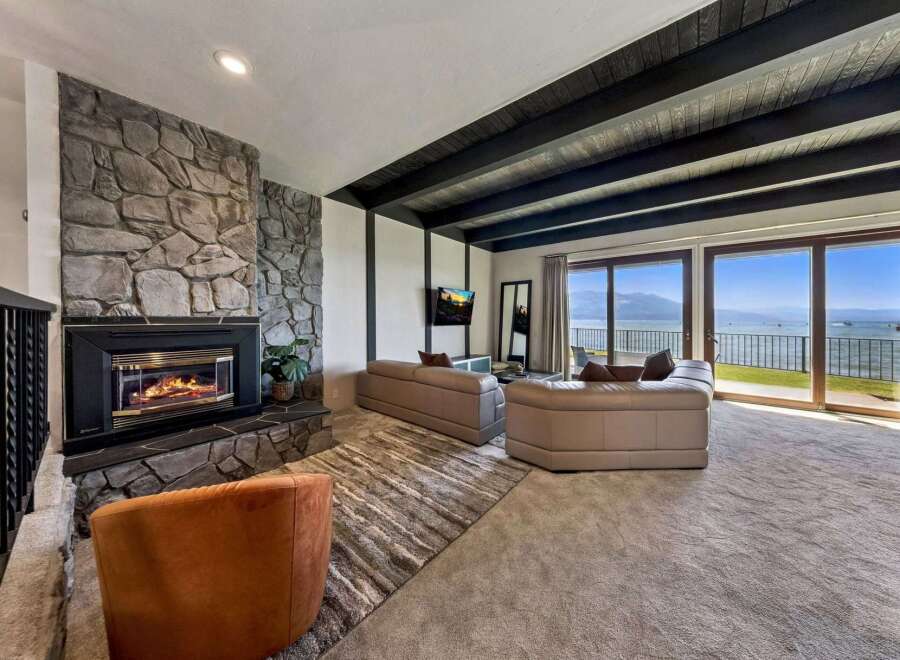 Experience breathtaking lake views from this stunning living room, featuring a grand stone fireplace and expansive sliding glass doors that open to a picturesque waterfront.