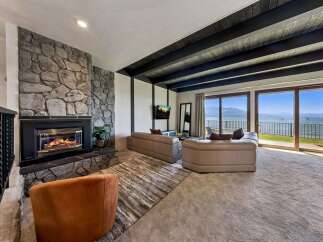 Experience breathtaking lake views from this stunning living room, featuring a grand stone fireplace and expansive sliding glass doors that open to a picturesque waterfront.