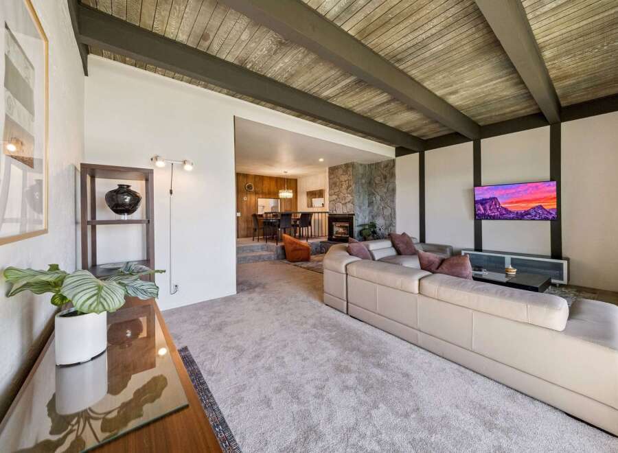 Experience modern living in this stunning home featuring a spacious living area with a beamed wood ceiling and a cozy stone fireplace.