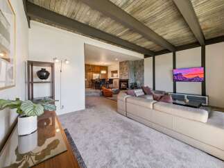 Experience modern living in this stunning home featuring a spacious living area with a beamed wood ceiling and a cozy stone fireplace.