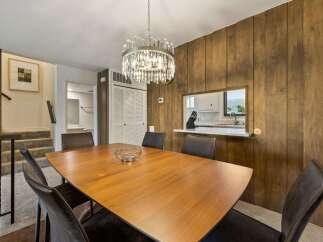 This dining room features a warm and inviting atmosphere with its rich wood-paneled walls and a stylish modern chandelier.