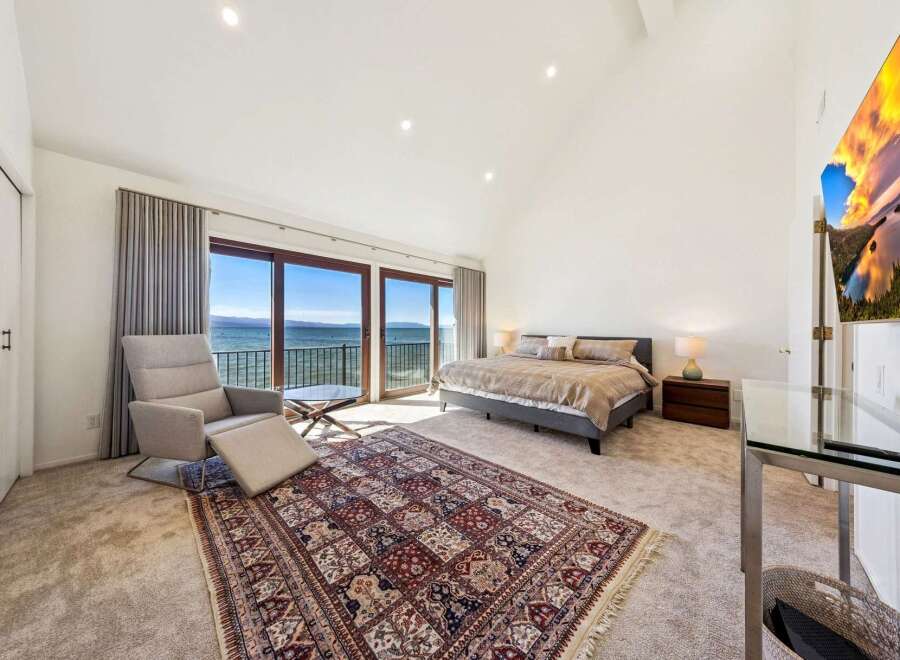 Experience breathtaking lake views from this luxurious master suite, featuring a comfortable recliner and a large bed.