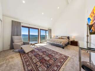 Experience breathtaking lake views from this luxurious master suite, featuring a comfortable recliner and a large bed.