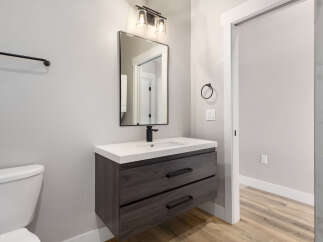 This modern bathroom features a sleek dark wood vanity with a white countertop and a black faucet, complemented by a minimalist black-framed mirror and a stylish dual-light fixture above.
