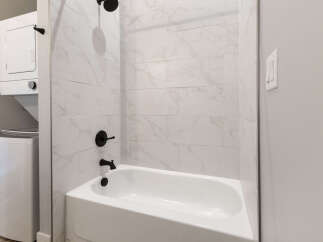 This modern bathroom features a sleek white bathtub with elegant marble-patterned tile walls and black fixtures.