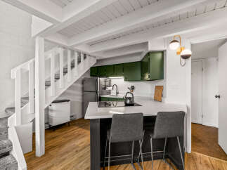 Discover this charming kitchen featuring sleek green cabinetry and a modern quartz countertop island, perfect for casual dining.