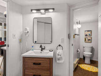 This modern bathroom features a sleek vanity with a dark wood finish and black hardware, complemented by a minimalist black-framed mirror and a stylish vanity light.