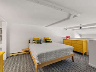 This charming bedroom features a comfortable queen-size bed with a light gray quilted comforter and decorative pillows.
