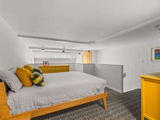 Discover this charming loft bedroom featuring a comfortable bed adorned with vibrant yellow and plaid pillows.