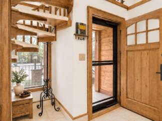 Step into this charming entryway featuring a rustic wooden spiral staircase with carpeted treads, perfect for a cozy cabin aesthetic.