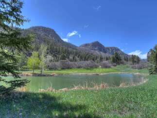 Experience the serene beauty of this golf course property, featuring a tranquil lake reflecting the majestic mountains and clear blue sky.