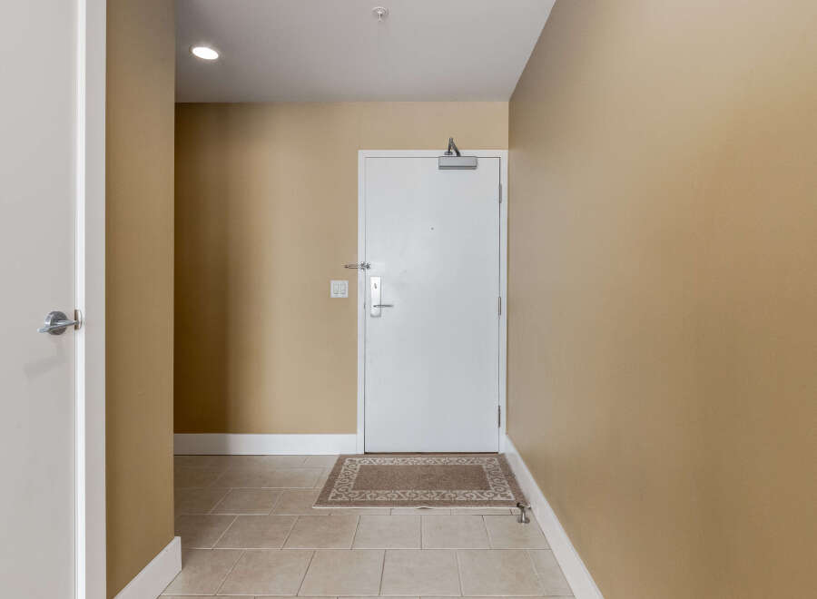 Step into this inviting entryway featuring a sleek white door with a modern silver handle, complemented by warm beige walls and a neutral-toned rug.