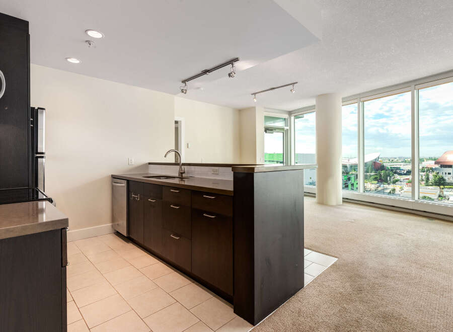 Experience modern living in this spacious condo featuring a sleek, dark wood kitchen island with a stainless steel sink and ample cabinetry.
