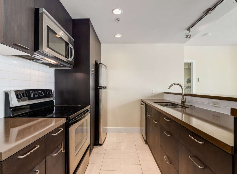 This modern kitchen features dark wood cabinetry and sleek stainless steel appliances, including a microwave, oven, and refrigerator.