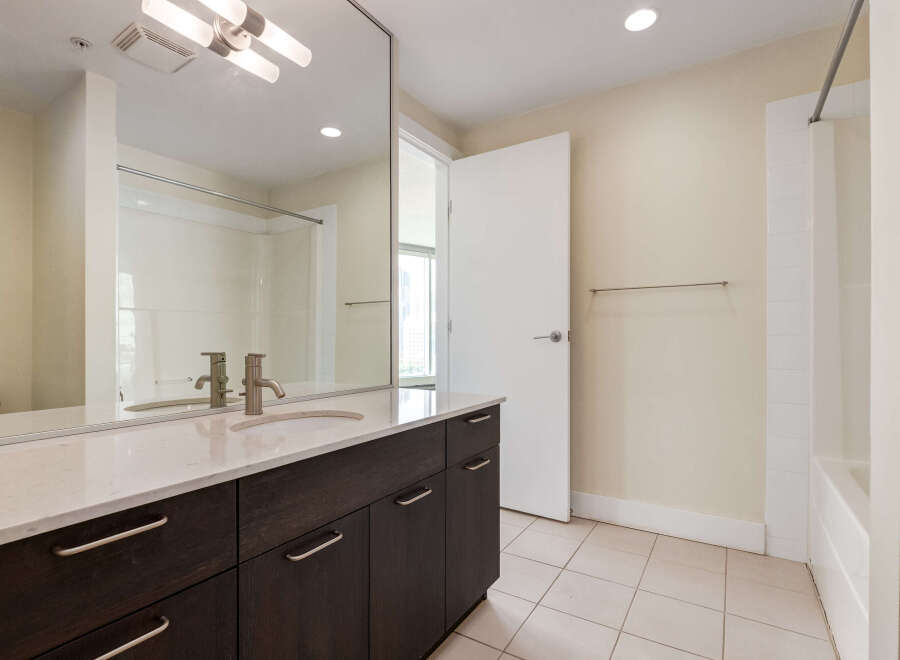 This modern bathroom features a sleek vanity with a marble countertop and dark wood cabinetry, complemented by a large mirror reflecting the shower area.