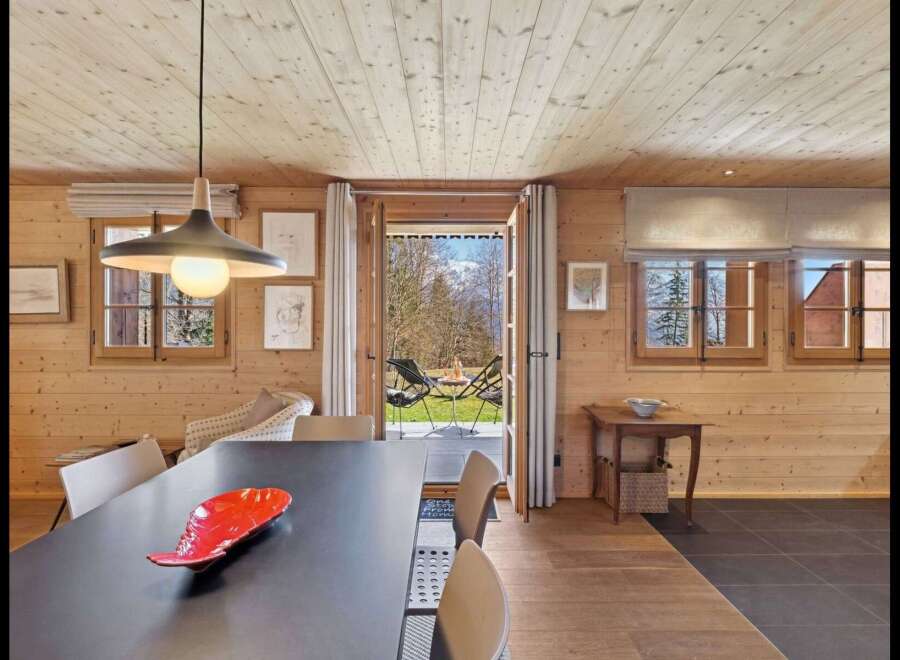 Experience cozy living in this charming wooden cabin, featuring a spacious dining area with a modern pendant light and a direct view to the outdoors.
