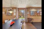 Experience cozy living in this charming wooden cabin, featuring a spacious dining area with a modern pendant light and a direct view to the outdoors.
